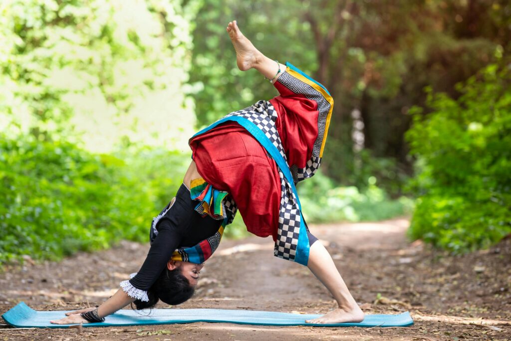 Woman practicing yoga outdoors in vibrant traditional clothing, showcasing flexibility and harmony with nature.